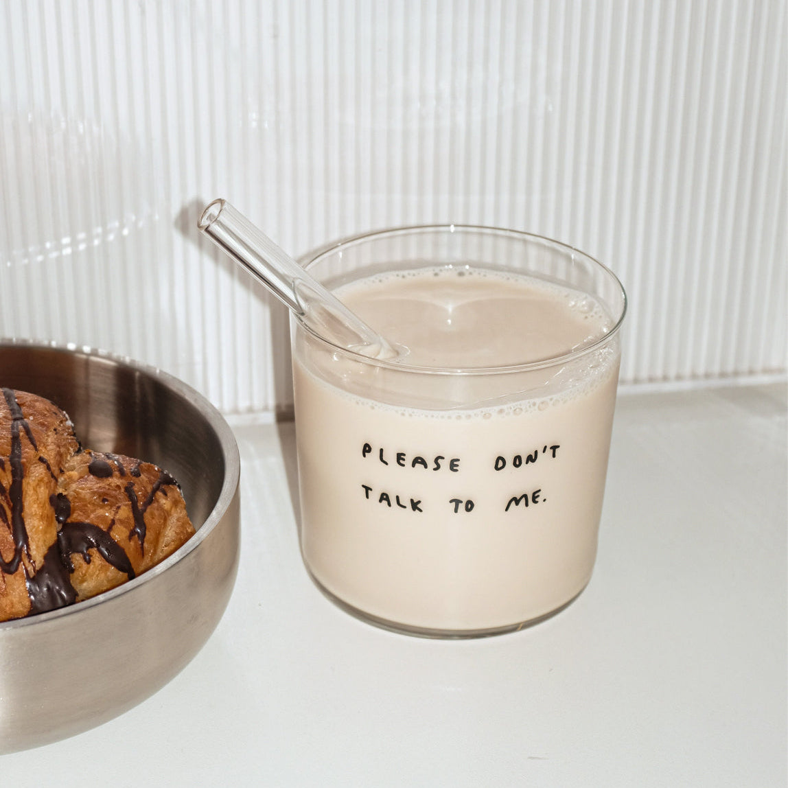 Wasserglas mit dem Schriftzug "Please dont talk to me". Das Glas ist mit Milch und einem Strohhalm befüllt.