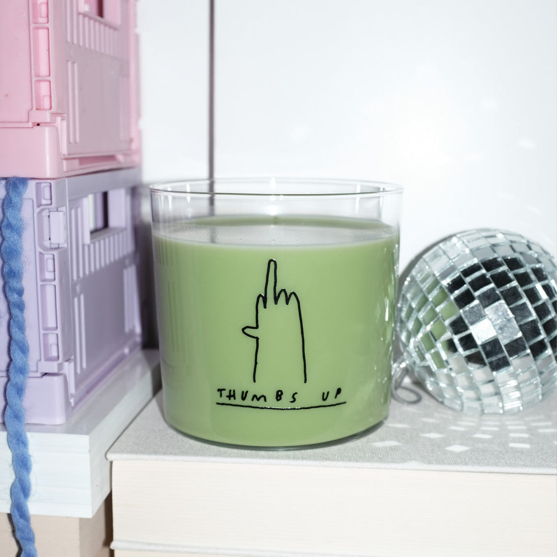 Wasserglas mit dem Motiv thumbs up. Dazu eine Hand die den Mittelfinger zeigt. Das Glas ist befüllt und steht neben einer kleinen Diskokugeln auf Büchern.
