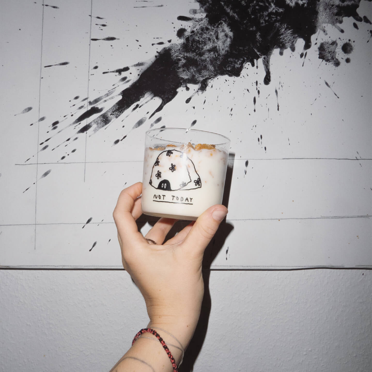 Klares, zylindrisches Trinkglas mit schwarzem, handschriftlich wirkendem Text. Darauf steht „not today", dazu eine Illustration von einer Figur, die unter einer Decke liegt. Man sieht nur die Augen der Figur die unter der Decke hervorschauen.

Das Glas von einer Hand vor eine weiße Wand gehalten und ist mit Milch und Cornflakes befüllt. 