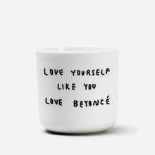 Weißer henkelloser Porzellan-Becher mit einer einfachen schwarzen Illustration, einem handschriftlichen Text der besagt "LOVE YOURSELF LIKE YOU LOVE BEYONCÉ" auf weißen Hintergrund.