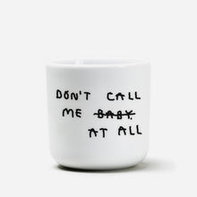 Weißer henkelloser Porzellan-Becher mit schwarzen Text „don't call me at baby" - das Baby ist durchgestrichen und durch "at all" ersetzt. Zu Deutsch (Nenn mich nicht Baby, bzw. Ruf mich nicht an).

Der Becher ist auf weißem Hintergrund.