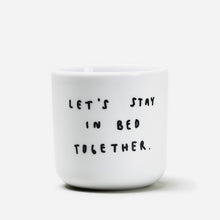 Weißer henkelloser Porzellan-Becher mit einer einfachen schwarzen Illustration, einem handschriftlichen Text der besagt "LET'S STAY IN BED TOGETHER" auf weißen Hintergrund.