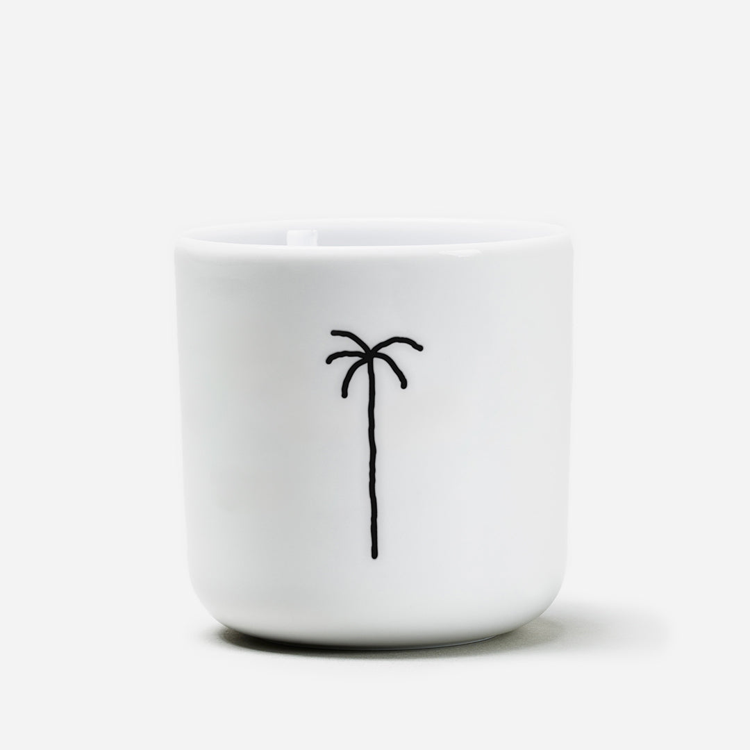 Weißer Becher aus Porzellan, Mittelgroß mit schwarzer Illustration einer Palme. Weißer Hintergrund.