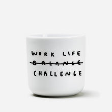 Weißer henkelloser Porzellan-Becher mit einer einfachen schwarzen Illustration, einem handschriftlichen Text der besagt "WORK LIFE CHALLENGE" wobei auch das Wort Balance dabeisteht und humorvoll durchgestrichen wird, dadurch von Challenge ersetzt wird. Auf weißen Hintergrund.