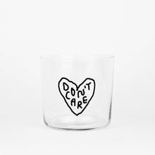 Transparentes Medium Designer Glas mit schwarzem Schriftzug "DON'T CARE" in einem Herz mit dünnen Wänden und Boden. Das Glas steht vor weißem Hintergrund.