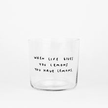 Transparentes Medium Designer Glas mit schwarzem Schriftzug "when life gives you lemons". Der Text ist auf weißen Hintergrund.