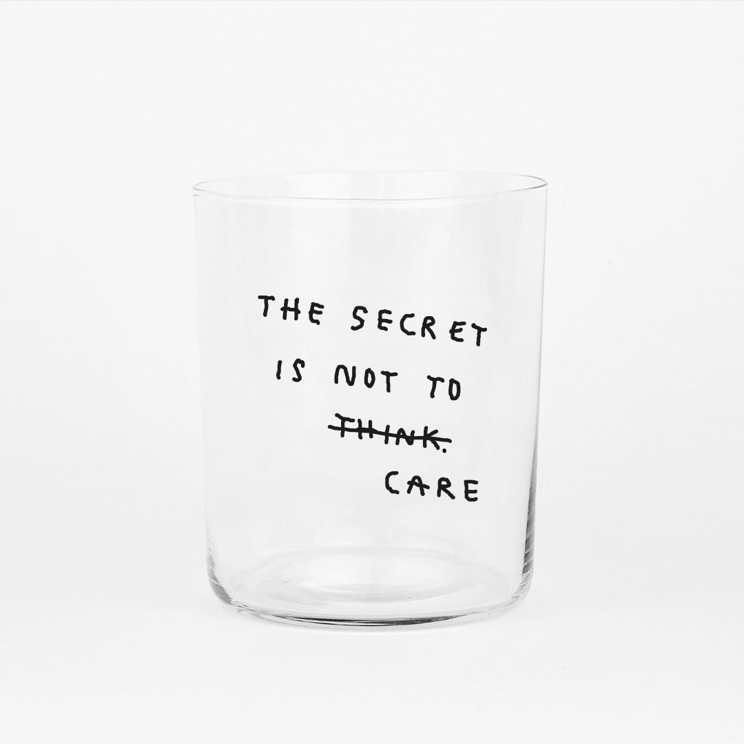 Großes Designer-Trinkglas mit sehr dünnen Glaswänden und einer schwarzen, einfarbigen Illustration auf der Vorderseite. Das Motiv auf dem Glas ist eine Handschrift in Schwarz in der geschrieben ist The secret is not to think wobei das think durchgestrichen ist und drunter das Wort CARE steht, auf weißem Hintergrund.