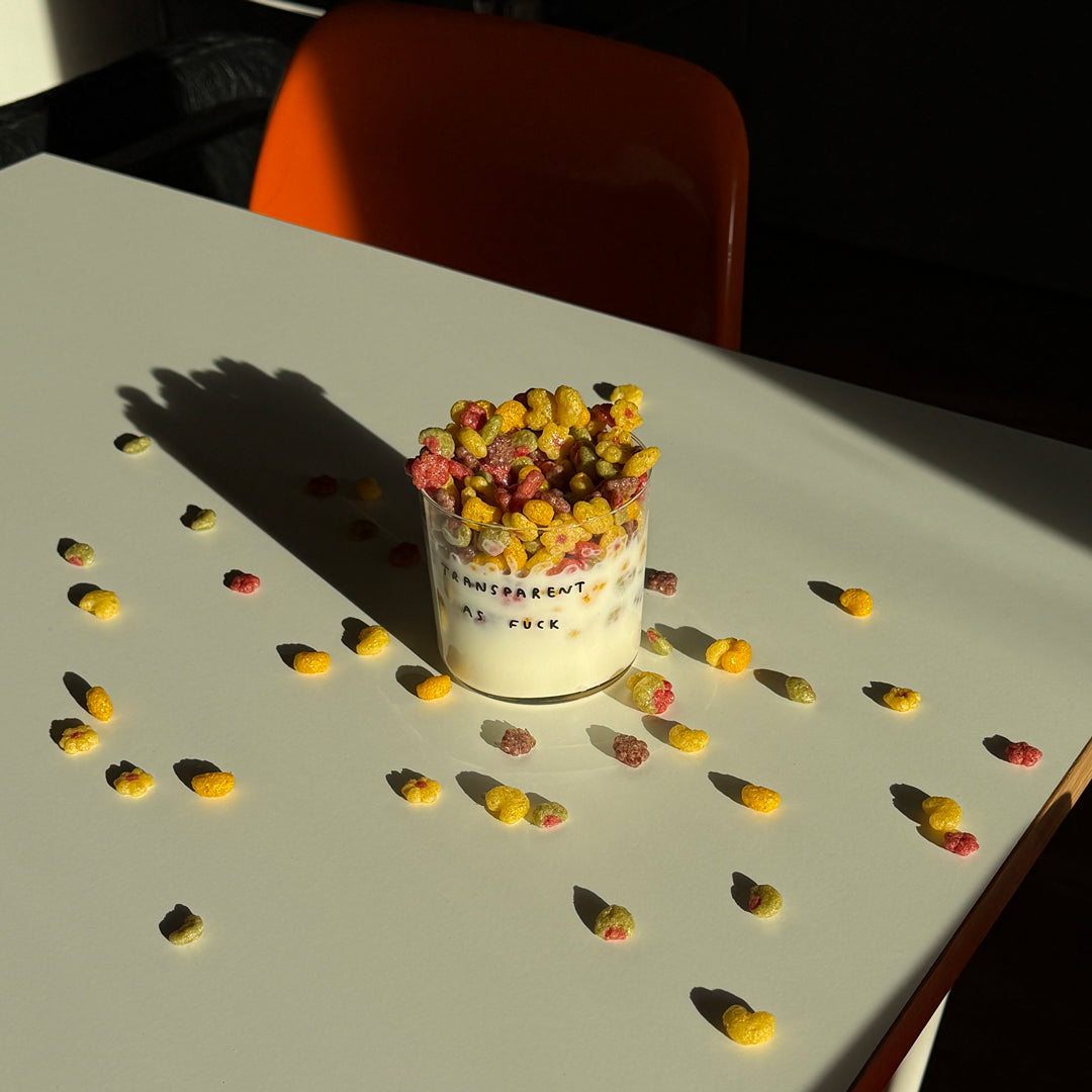 Medium Designer-Trinkglas mit sehr dünnen Glaswänden und einer schwarzen, einfarbigen Illustration auf der Vorderseite. Das Motiv zeigt eine Typografie in der geschrieben ist TRANSPARENT AS FUCK.

Das Glas steht auf einem weißen Tisch mit orangenen Stuhl im Hintergrund. Das Glas ist mit viel Milch und COrnflakes befüllt. 
