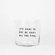 Transparentes Medium Designer Glas mit schwarzem Schriftzug "It's okay to not be okay all the time" mit dünnen Wänden und Boden. 

Das Glas ist ungefüllt vor grauem Hintergrund. 