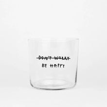 Transparentes Medium Designer Glas mit schwarzem Schriftzug "Don't worry be happy" mit dünnen Wänden und Boden. 

Das Glas ist ungefüllt vor grauem Hintergrund. 