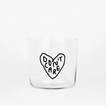 Transparentes Medium Designer Glas mit schwarzem Schriftzug "DON'T CARE" in einem Herz mit dünnen Wänden und Boden. Das Glas steht vor weißem Hintergrund.