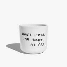 Weißer henkelloser Porzellan-Becher mit schwarzen Text „don't call me at baby" - das Baby ist durchgestrichen und durch "at all" ersetzt. Zu Deutsch (Nenn mich nicht Baby, bzw. Ruf mich nicht an).

Der Becher ist auf weißem Hintergrund.