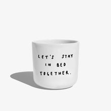 Weißer henkelloser Porzellan-Becher mit einer einfachen schwarzen Illustration, einem handschriftlichen Text der besagt "LET'S STAY IN BED TOGETHER" auf weißen Hintergrund.