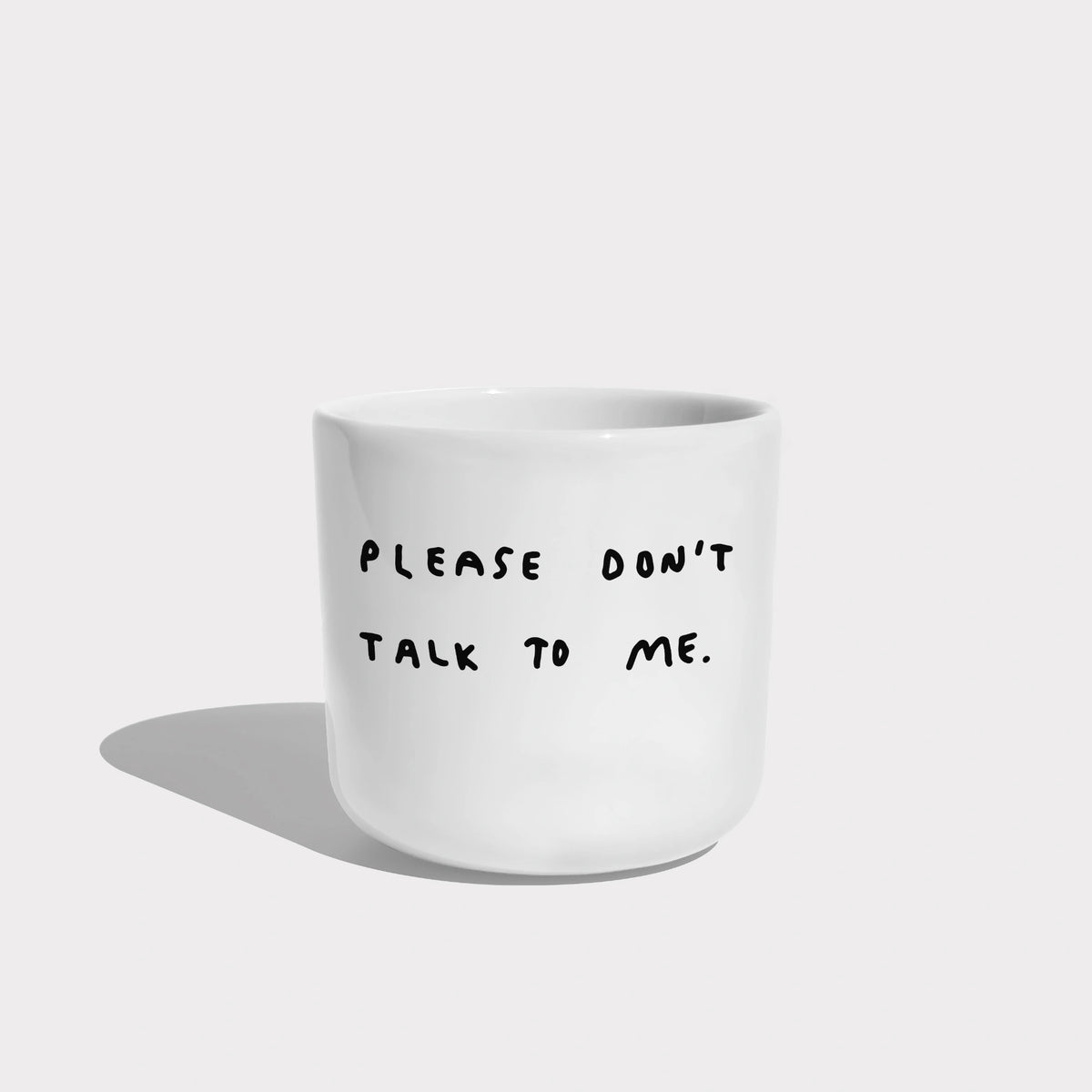 Weißer henkelloser Porzellan-Becher mit einer einfachen schwarzen Illustration, einem handschriftlichen Text der besagt "PLEASE DON'T TALK TO ME" auf weißen Hintergrund.