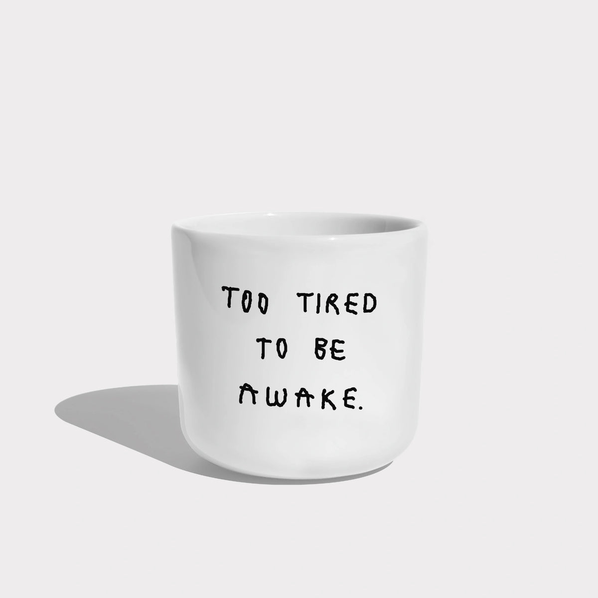 Weißer henkelloser Porzellan-Becher mit schwarzen Text „Too tired to be awake"

Der Becher ist auf weißem Hintergrund.