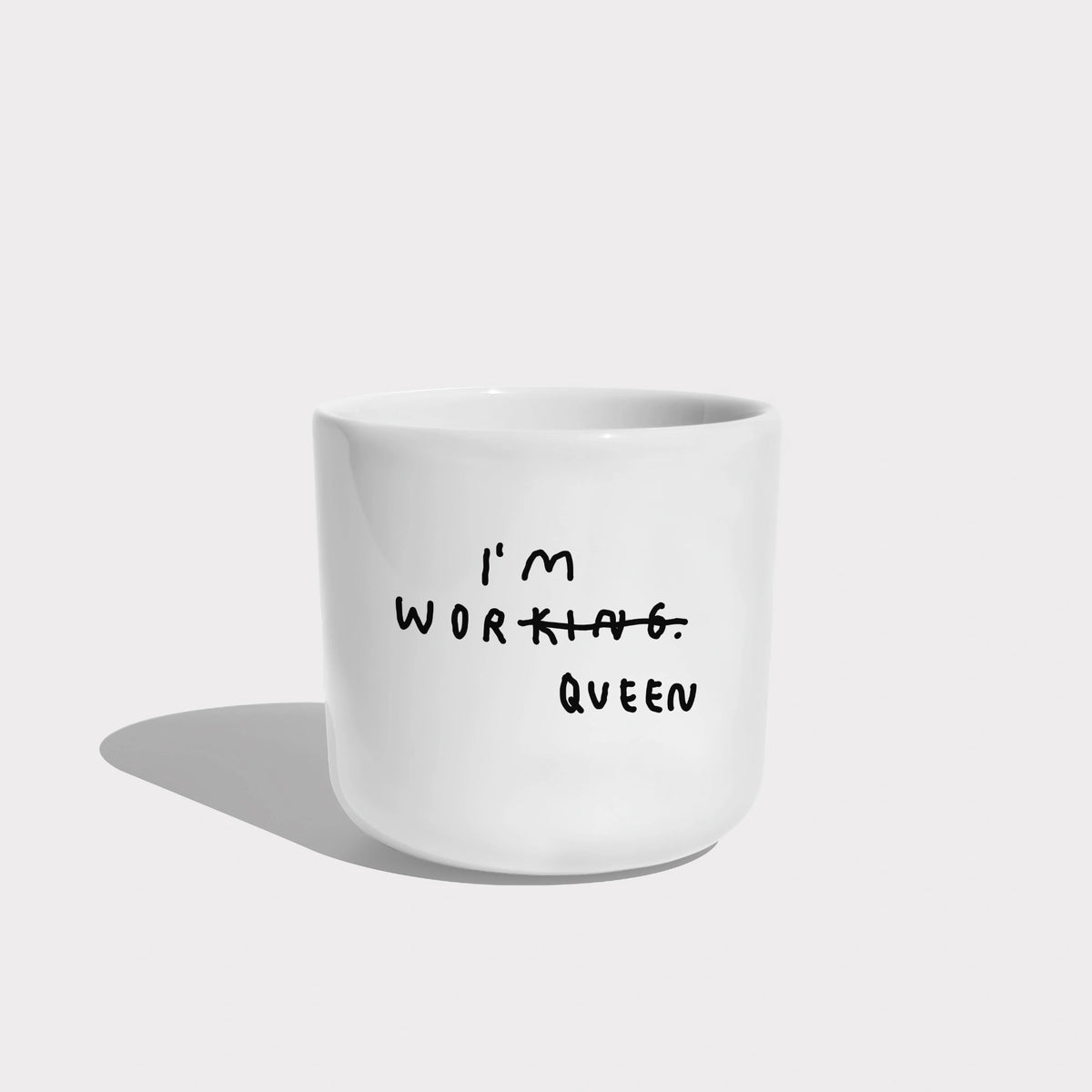 Weißer henkelloser Porzellan-Becher, Mittelgroß mit schwarzem Spruch "I'm Worqueen" - eigentlich mit dem Wort Working aber KING durchgestrichen und zu QUEEN gemacht. Weißer Hintergrund.