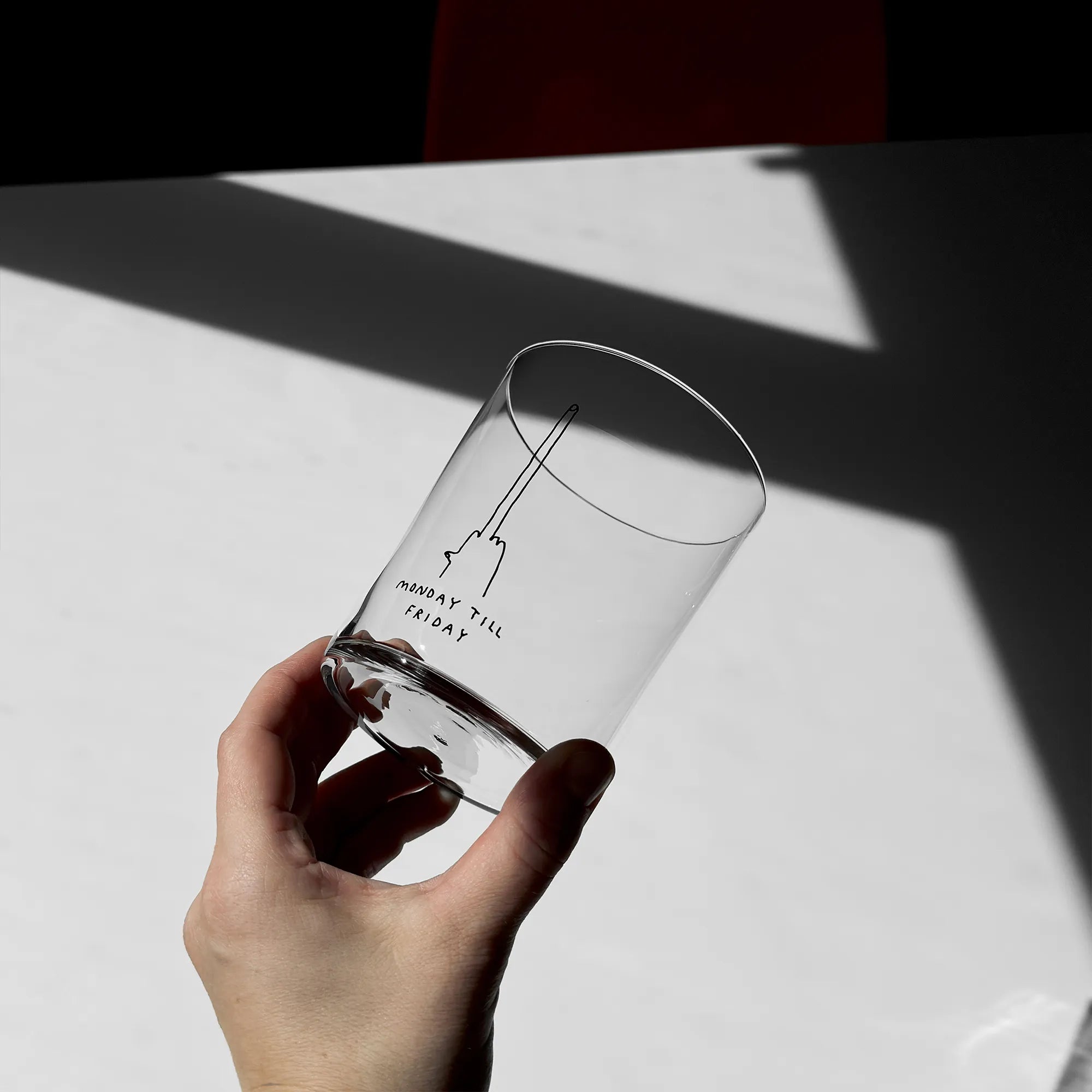 Großes Designer-Trinkglas mit sehr dünnen Glaswänden und einer schwarzen, einfarbigen Illustration auf der Vorderseite mit dem Motiv „Monday till Friday“. Illustration von Künstlerin, Illustratorin und Co-Gründerin Johanna Schwarzer.

Das Glas steht auf einem weißen Tisch, ist ungefüllt und liegt. Dabei wird es in der Hand gehalten, man sieht ein Tattoo und eine Kette. 