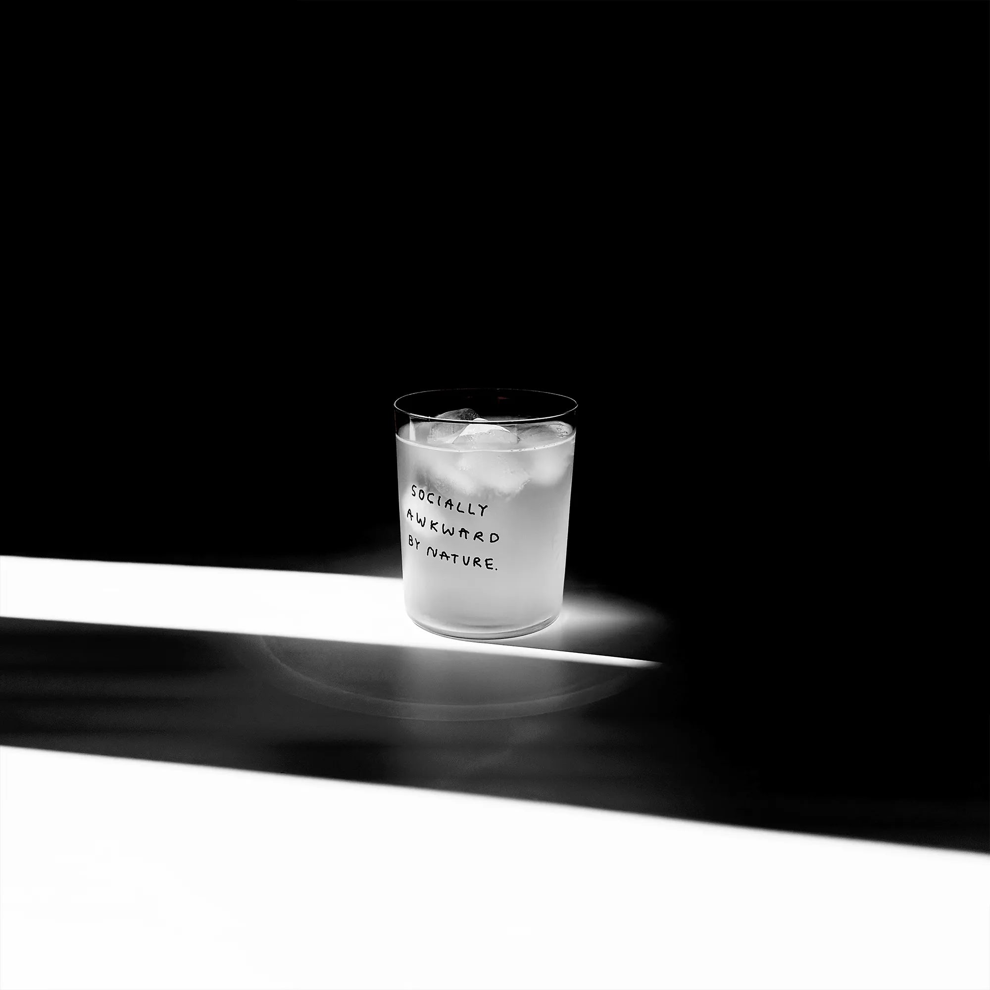 Großes Designer-Trinkglas mit sehr dünnen Glaswänden und einer schwarzen, einfarbigen Illustration auf der Vorderseite mit dem Motiv "Socially awkward by Nature“. Illustration von Künstlerin, Illustratorin und Co-Gründerin Johanna Schwarzer.

Das Glas steht auf einem weißen Tisch, das Foto ist in einer Nahaufnahme, das Glas ist mit einer weißen Flüssigkeit und Eiswürfeln befüllt.