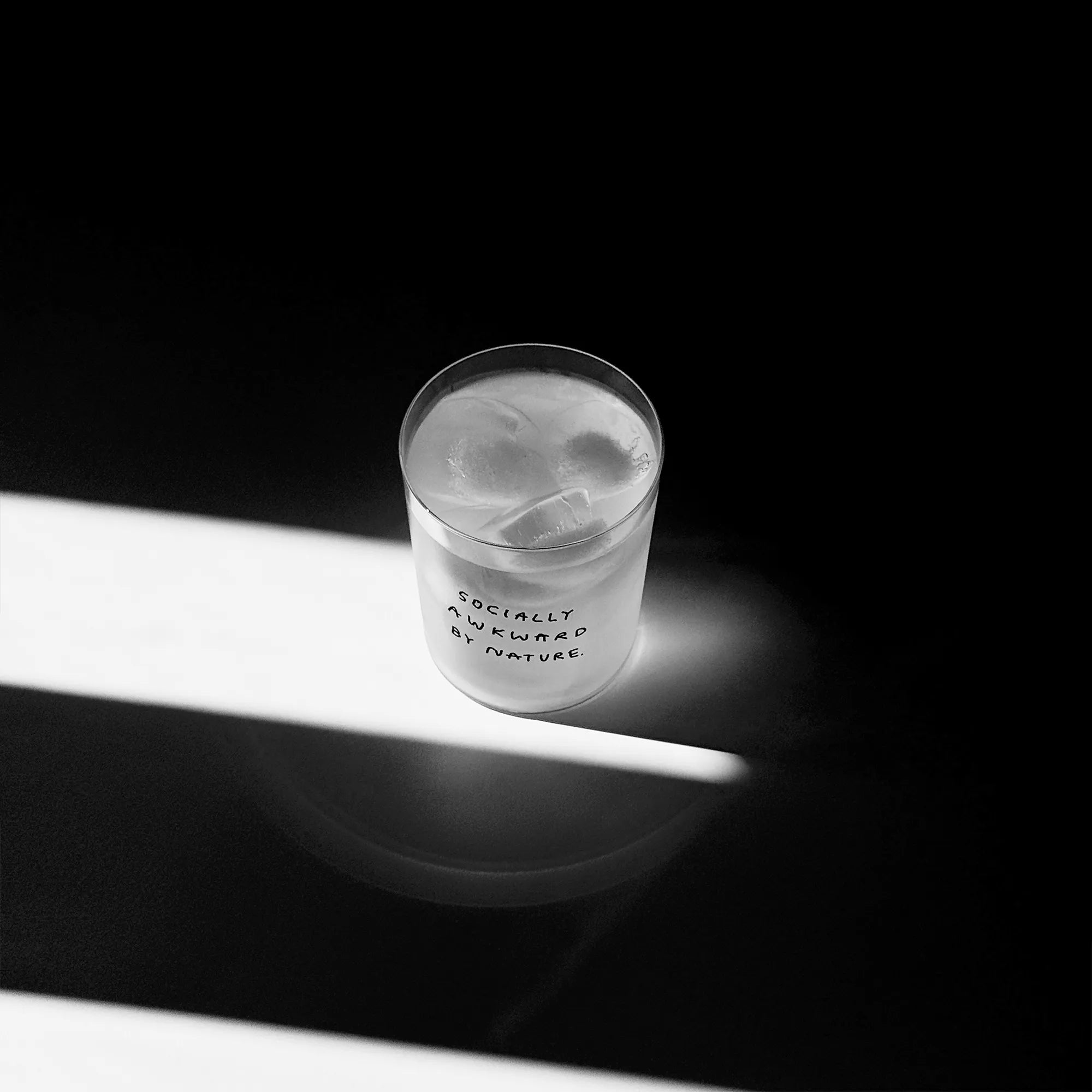 Großes Designer-Trinkglas mit sehr dünnen Glaswänden und einer schwarzen, einfarbigen Illustration auf der Vorderseite mit dem Motiv "Socially awkward by Nature“. Illustration von Künstlerin, Illustratorin und Co-Gründerin Johanna Schwarzer.

Das Glas steht auf einem weißen Tisch, das Foto ist in einer Nahaufnahme, das Glas ist mit einer weißen Flüssigkeit und Eiswürfeln befüllt.