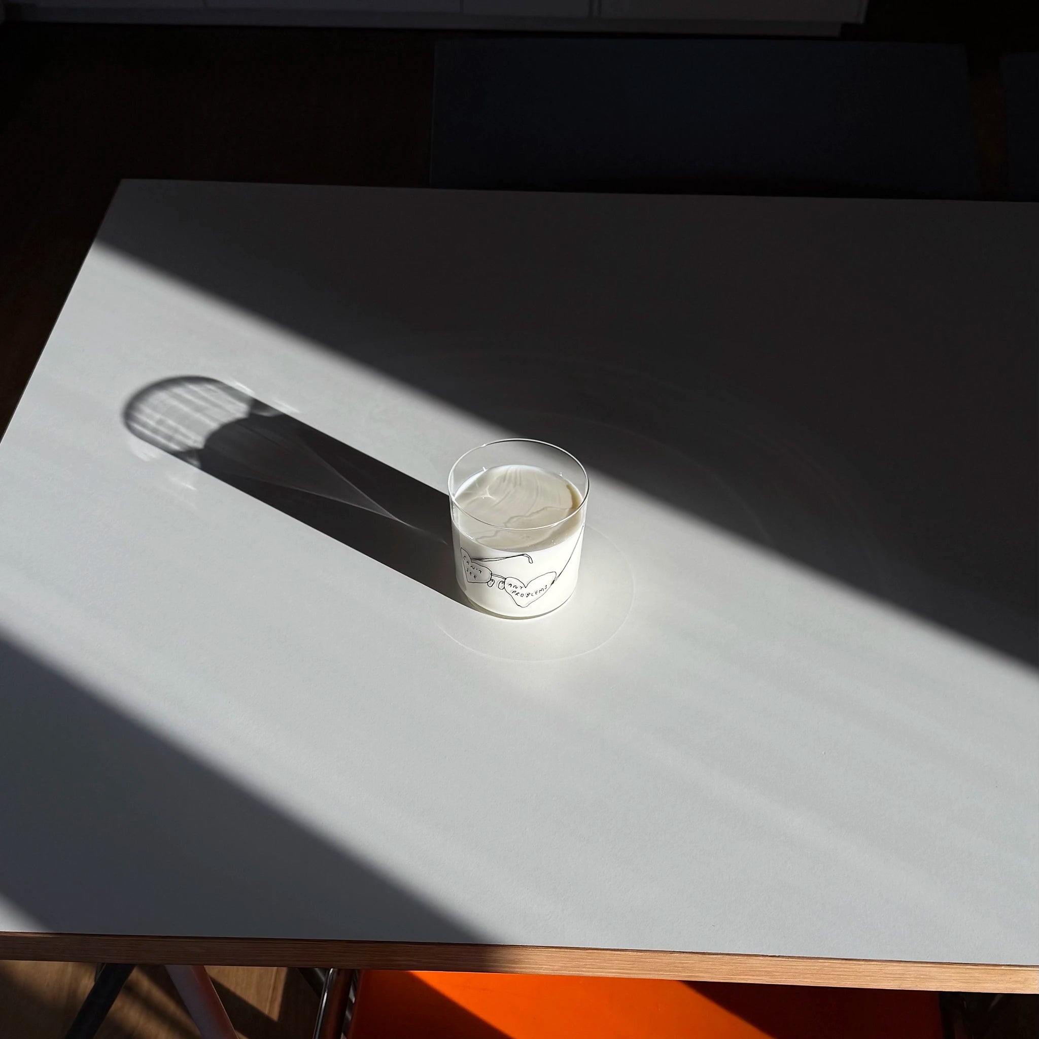 Transparentes Medium Designer Glas mit schwarzem Schriftzug "can't see any problems" mit einer Brille, die Brillengläser in herzformen hat. Das Glas steht auf seiner weißen Tischplatte in einem sehr milden Lichteinfall und wirft einen großen Schatten.
