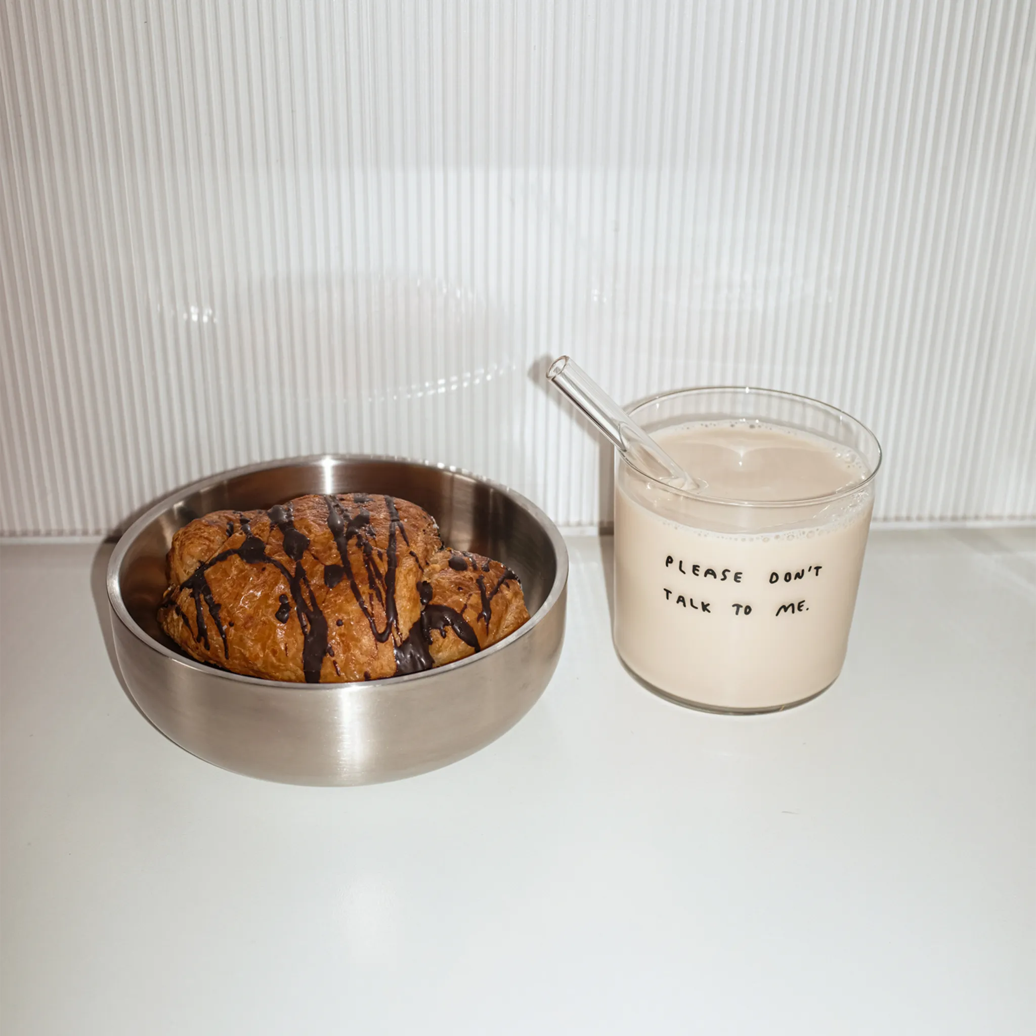 Wasserglas mit dem Schriftzug "Please dont talk to me". Das Glas ist mit Milch und einem Strohhalm befüllt. 