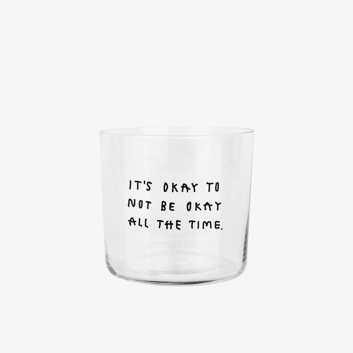 Transparentes Medium Designer Glas mit schwarzem Schriftzug "It's okay to not be okay all the time" mit dünnen Wänden und Boden. 

Das Glas ist ungefüllt vor grauem Hintergrund. 