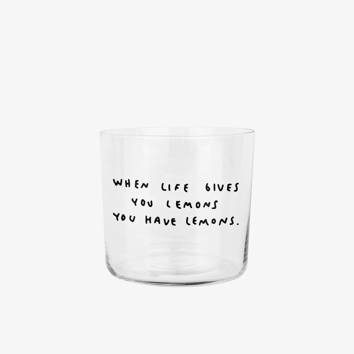 Transparentes Medium Designer Glas mit schwarzem Schriftzug "when life gives you lemons". Der Text ist auf weißen Hintergrund.