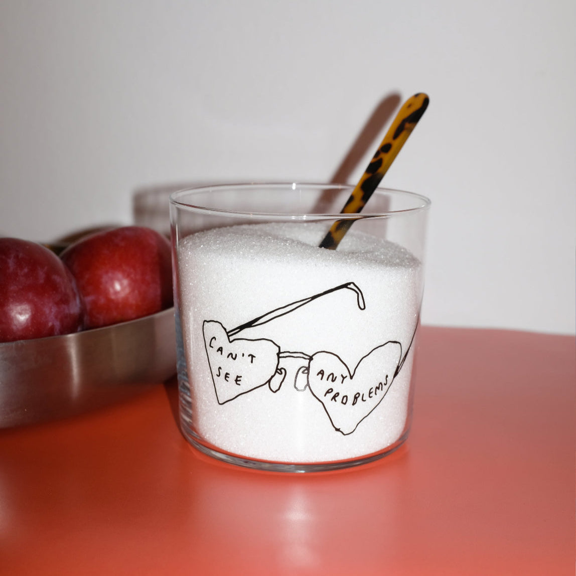 Wasserglas mit Schriftzug Cant see any problems. Das Glas steht auf einem Buch, zwei Äpfel liegen dahinter. Das Glas ist mit Zucker befüllt. 