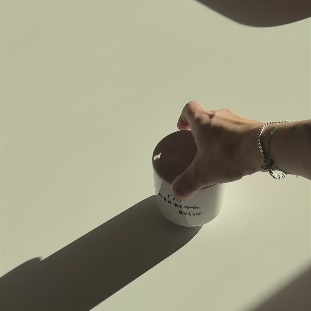 Weißer henkelloser Porzellan-Becher, Mittelgroß mit schwarzem Spruch "I'm Worqueen" - eigentlich mit dem Wort Working aber KING durchgestrichen und zu QUEEN gemacht. Weißer Hintergrund.

Der Becher wird in dem Video auf einen Tisch geschoben und mit tee befüllt. Zuletzt wird es wieder aus dem Video herausgehoben.