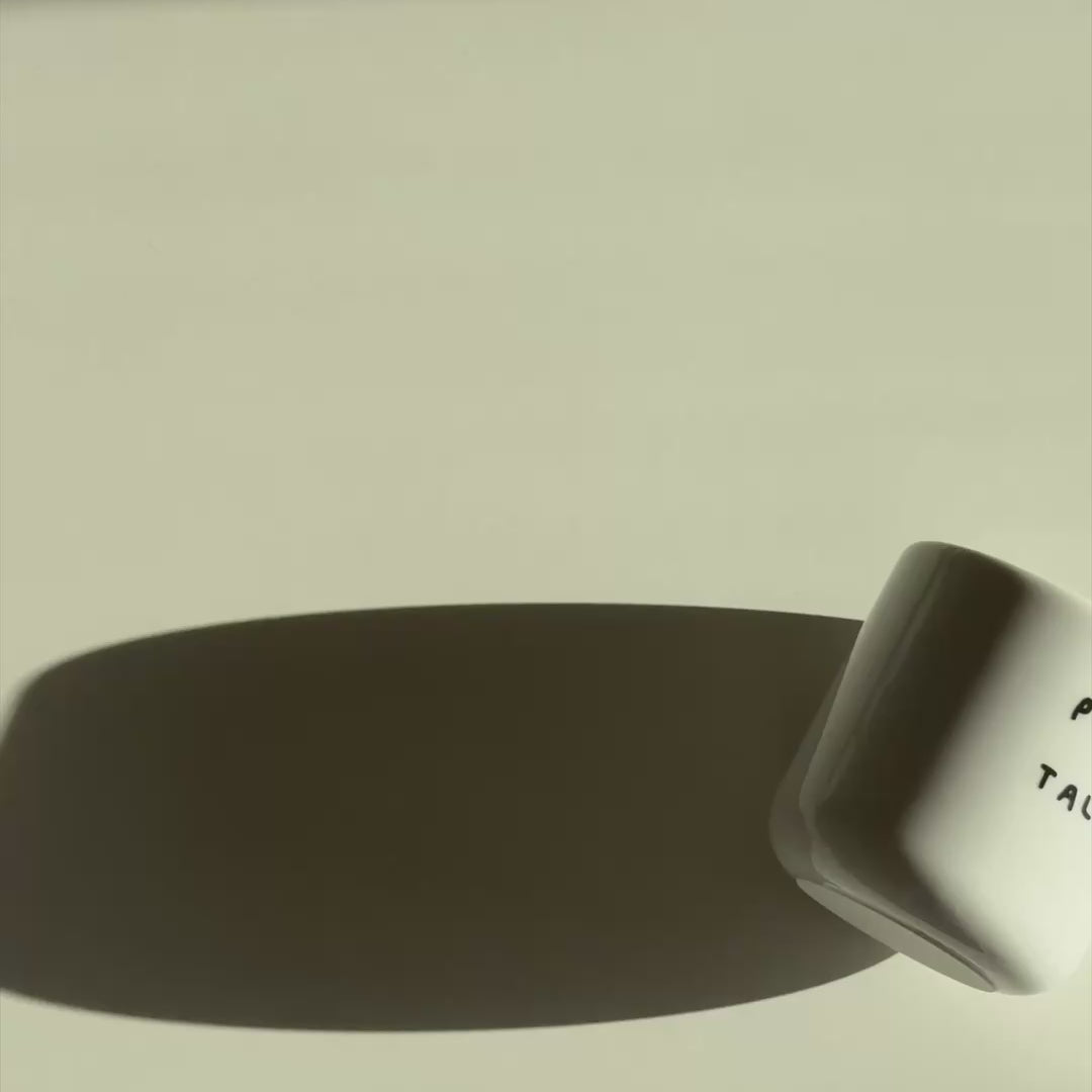 Weißer henkelloser Porzellan-Becher mit einer einfachen schwarzen Illustration, einem handschriftlichen Text der besagt "PLEASE DON'T TALK TO ME" auf weißen Hintergrund. Der Becher wird durch das Bild gerollt und dreht sich langsam durch das Video. 