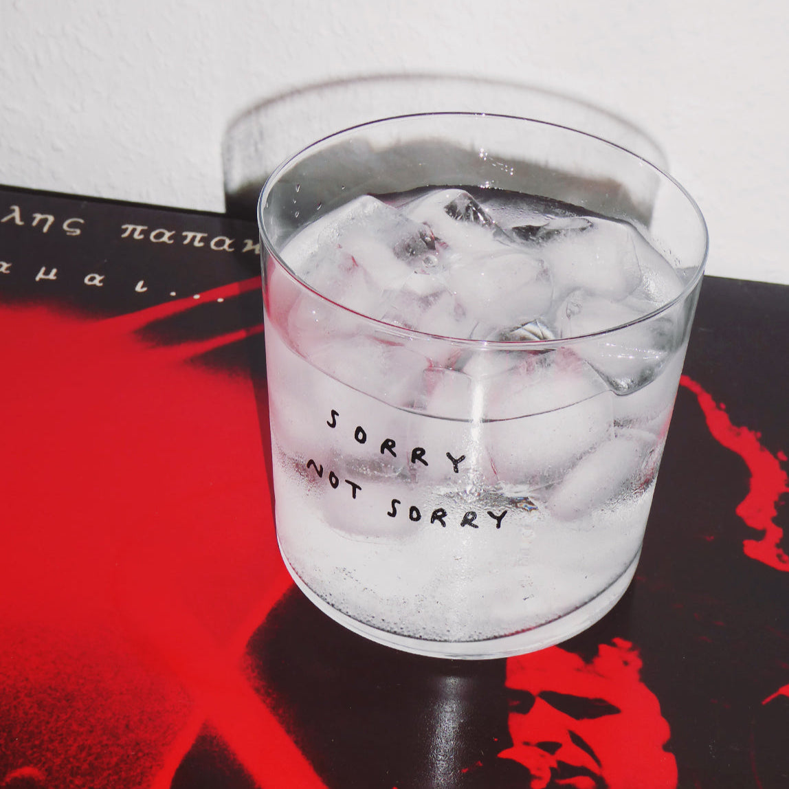 Wasserglas mit dem Motiv Sorry not sorry. Das Glas ist mit Wasser und Eiswürfeln befüllt und steht auf einem Buch.